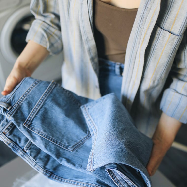 woman holds denim trousers ready to wash in front of washing machine