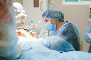 Female surgeon performs surgery in theatre on patient while nurse holds instrument above prone patient