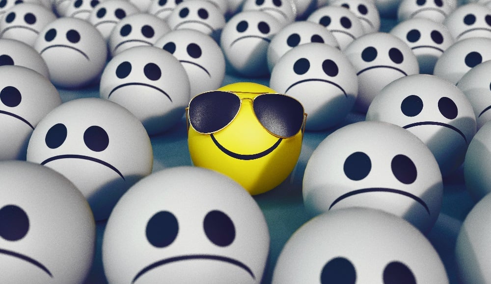 Illustration showing a yellow ball with smiley face and sunglasses amongst unhappy grey faces