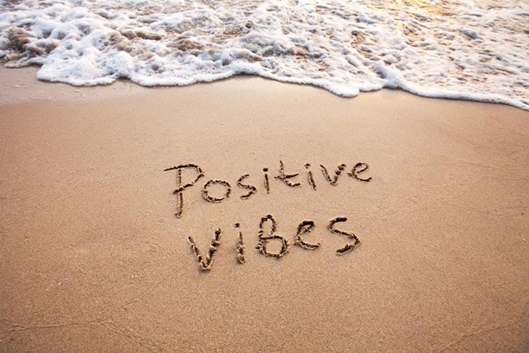 Positive vibes message written in the sand with waves