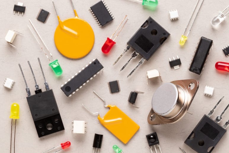 Electronic components on a beige background. There are microcontrollers, transistors, yellow and red LEDs, microcircuits, thyristors, capacitor.