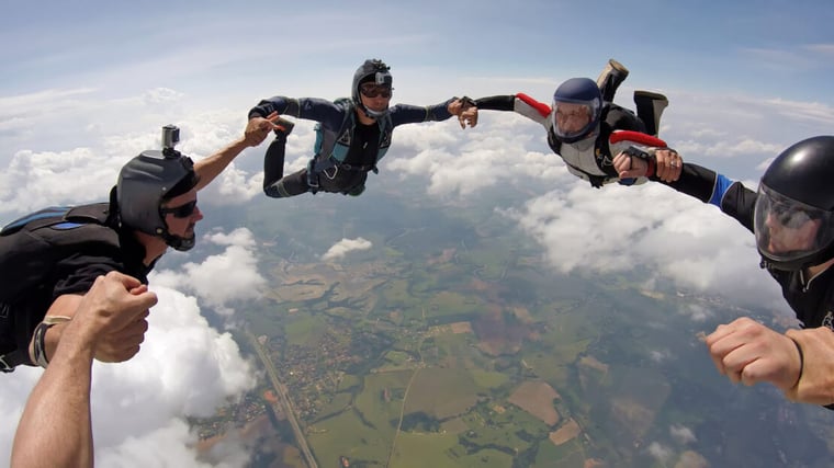 Skydivers in freefall form a ring with their hands signifying teamwork, group thinking and collaboration