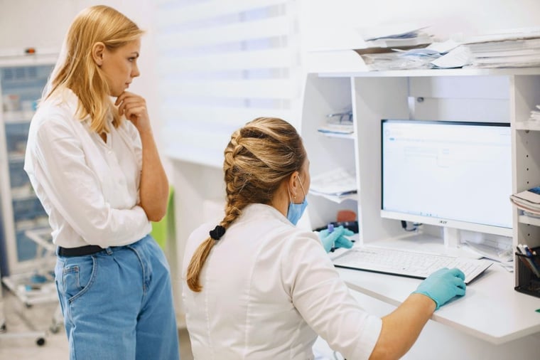 Two female medical researchers stand and sit before a computer screen analysing results
