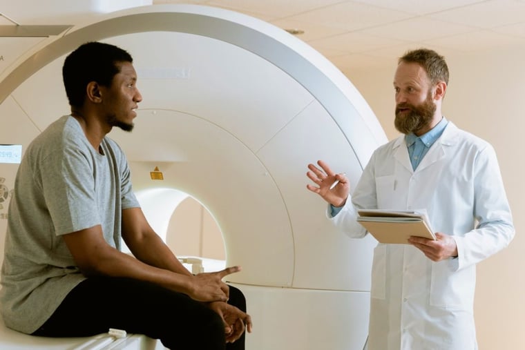 Patient sits on scanner bed while doctor with clipboard asks him questions while gesturing