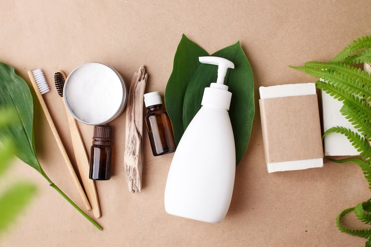 Plastic and glass hygiene product bottles lie on brown paper background with green leaves inbetween